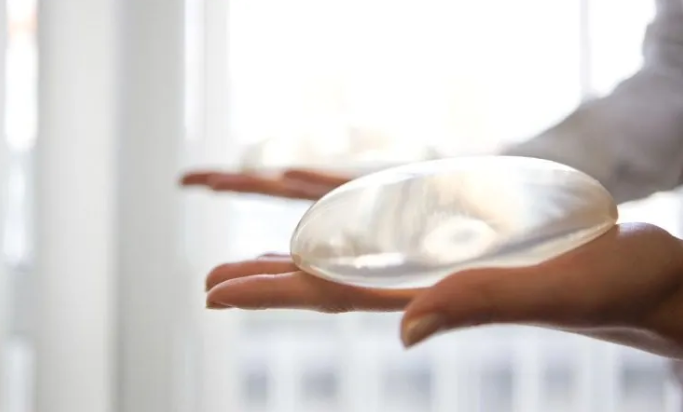 Hands holding a breast implant in light.