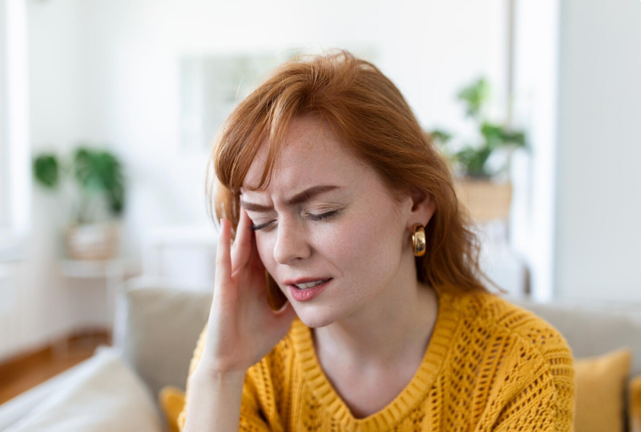 Woman with headache wearing yellow jumper indoors.