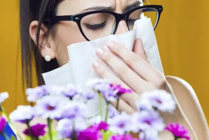 Woman sneezing near flowers, allergy season and histamine reaction
