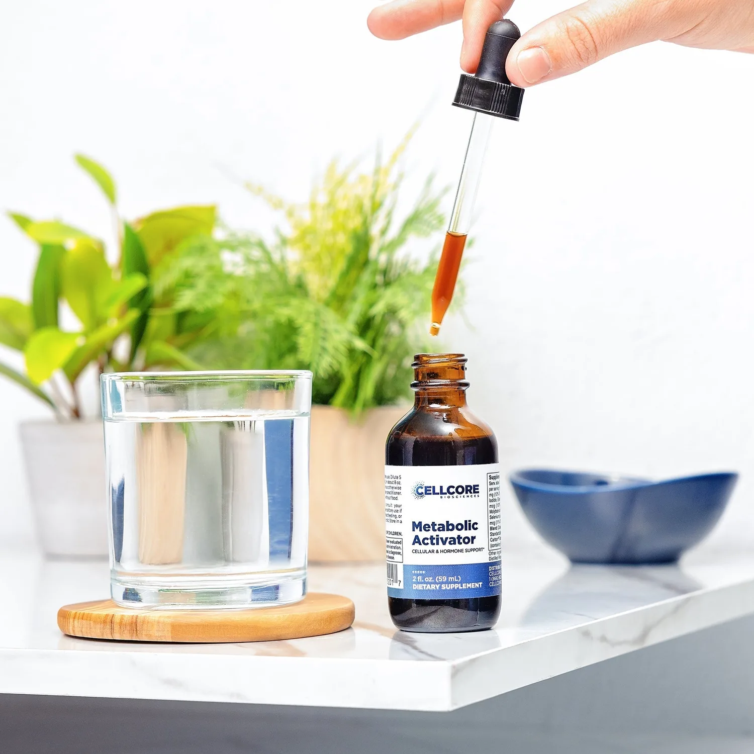 Metabolic Activator dropper bottle beside a glass of water, drops ready to be diluted